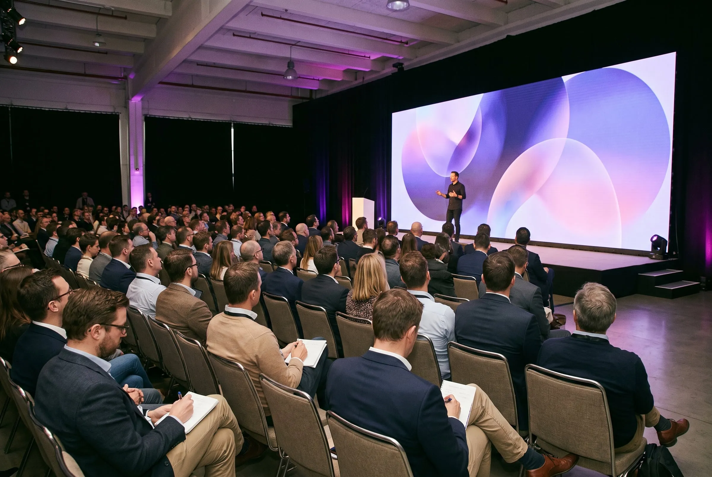 Publikum einer Marketing-Konferenz vor einer Bühne mit großer Leinwand